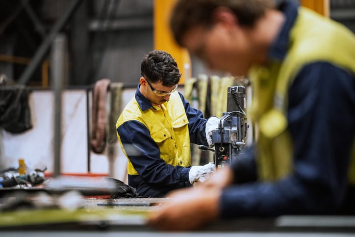 Qualified welders working on steel construction, grinding and welding iron parts in modern bright warehouse