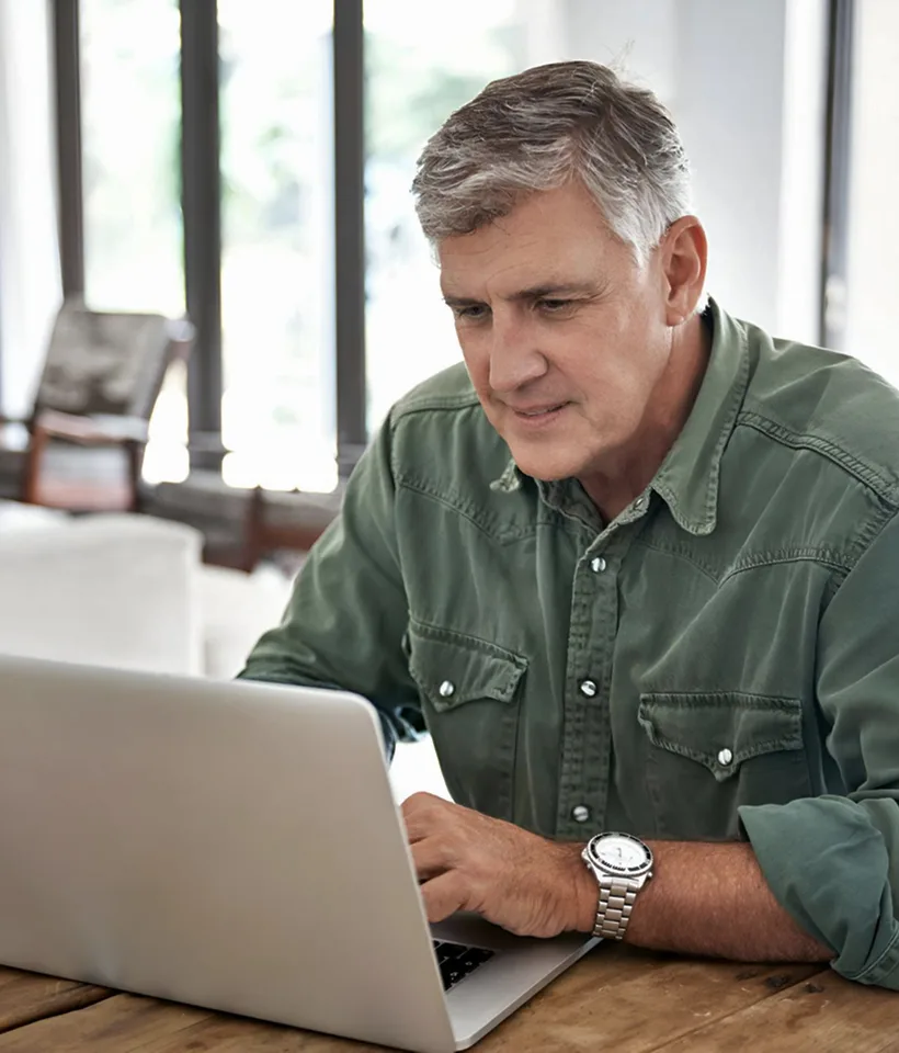 A man in a green shirt sits at a table, working on a laptop.